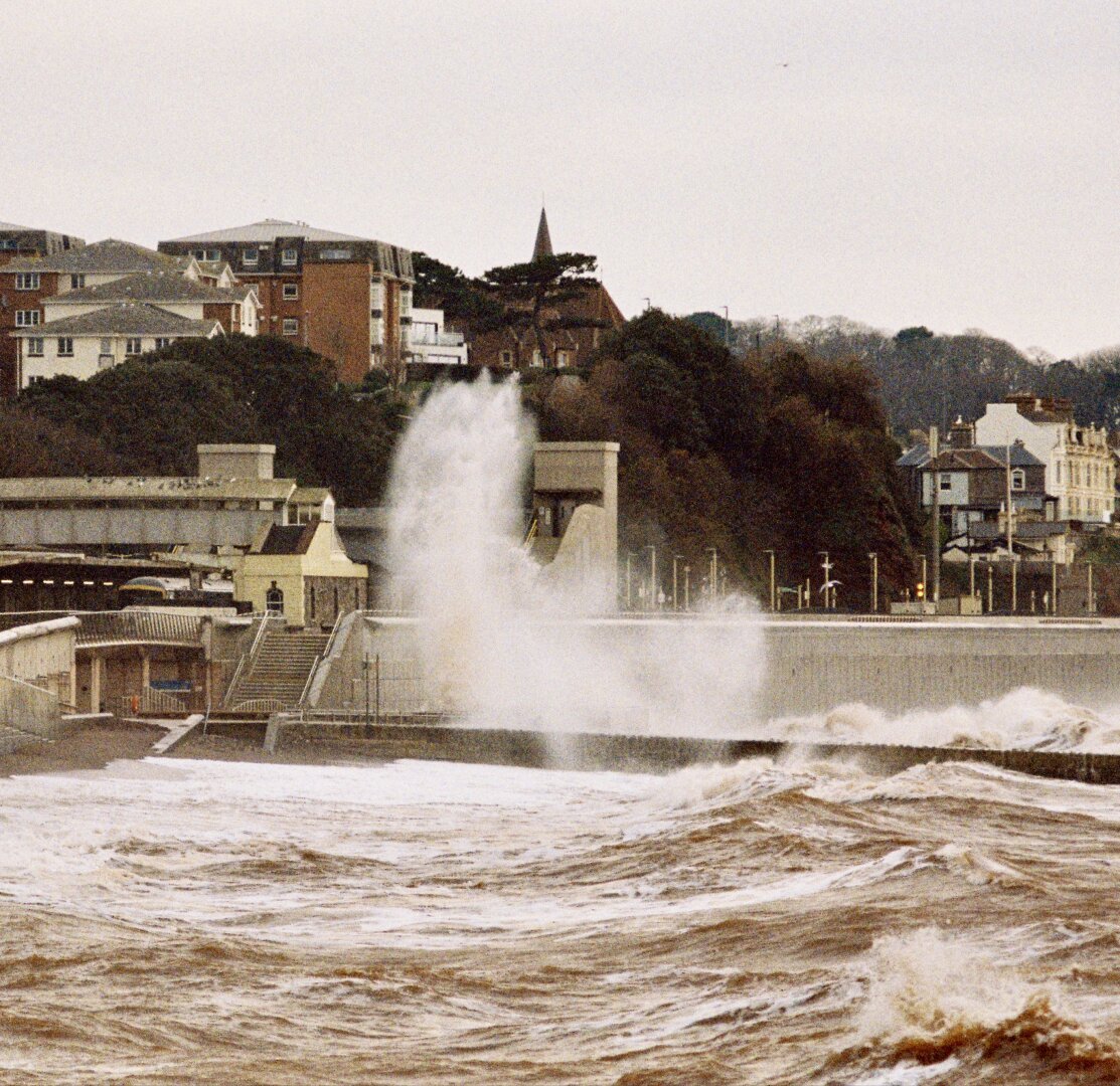 A wave breaking over the sea wall at Dawlish, the water stained red by the sand.