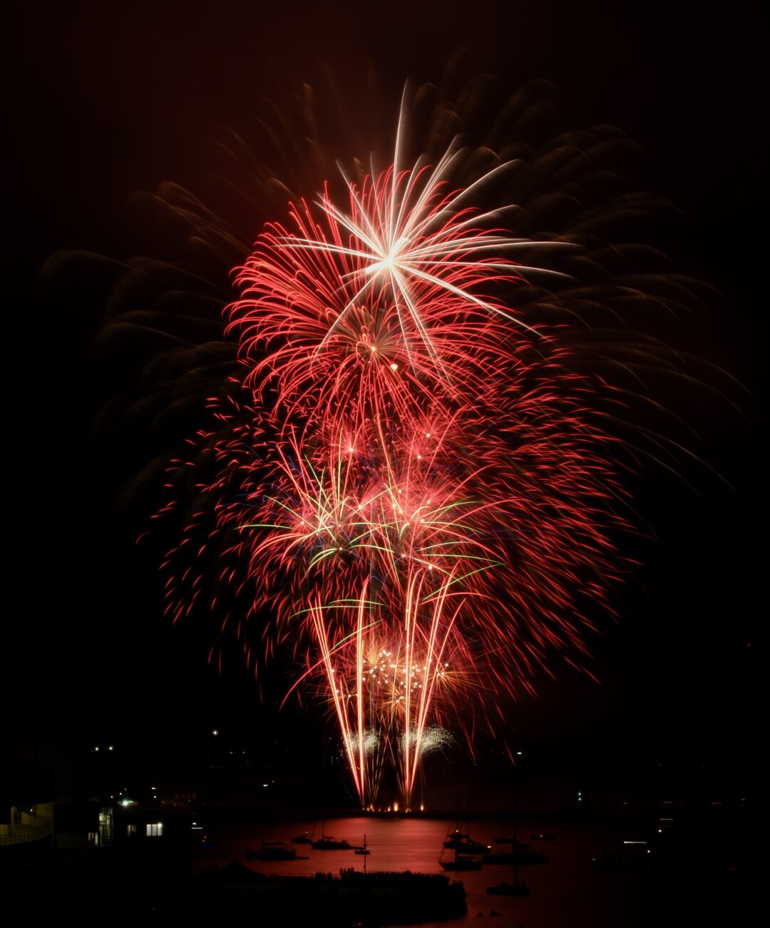Red fireworks bursting over water at night.